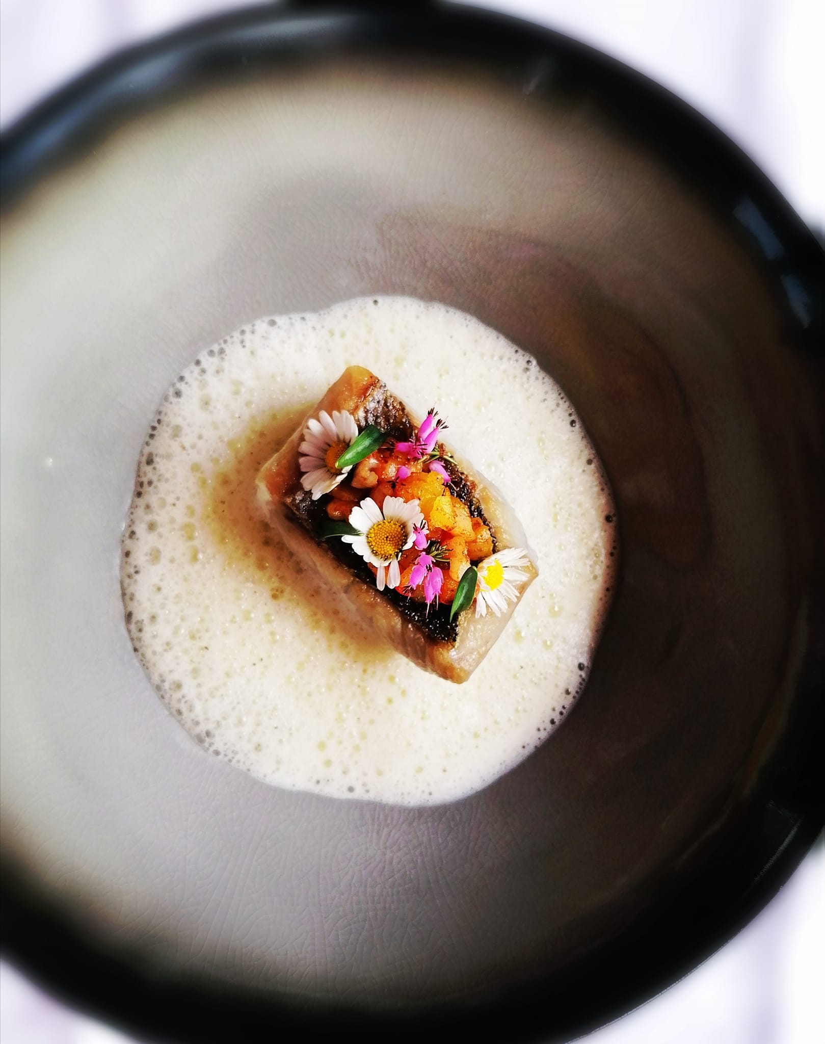 Gourmetgericht mit Schaum und essbaren Blüten auf dunklem Teller